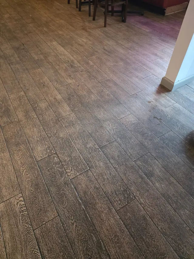A restaurant's wood-look floor before cleaning, dull and filmed with traffic